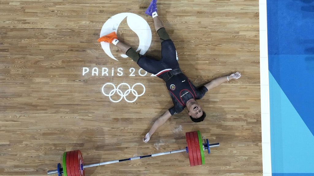 Lifter Indonesia, Rizki Juniansyah, berbaring telentang di panggung untuk merayakan keberhasilannya merebut medali emas pada cabang angkat besi kelas 73 kilogram putra Olimpiade Paris 2024, Jumat (9/8/2024) dini hari WIB, di South Paris Arena, Paris, Perancis.