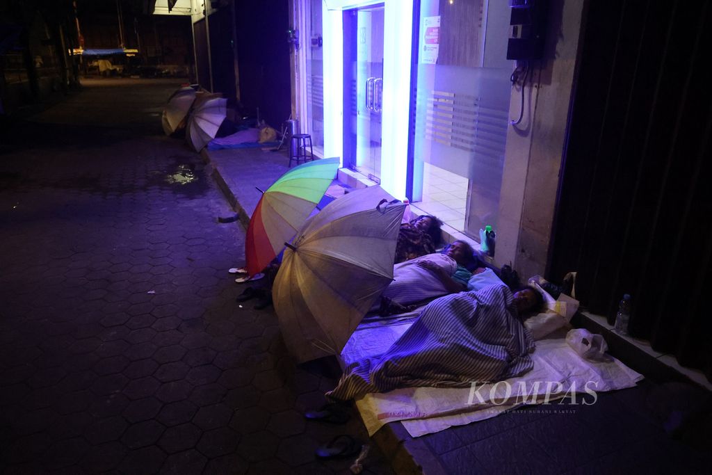 Buruh gendong tidur di depan sebuah bank di seberang Pasar Beringharjo, Yogyakarta, Selasa (7/3/2023) dini hari. 
