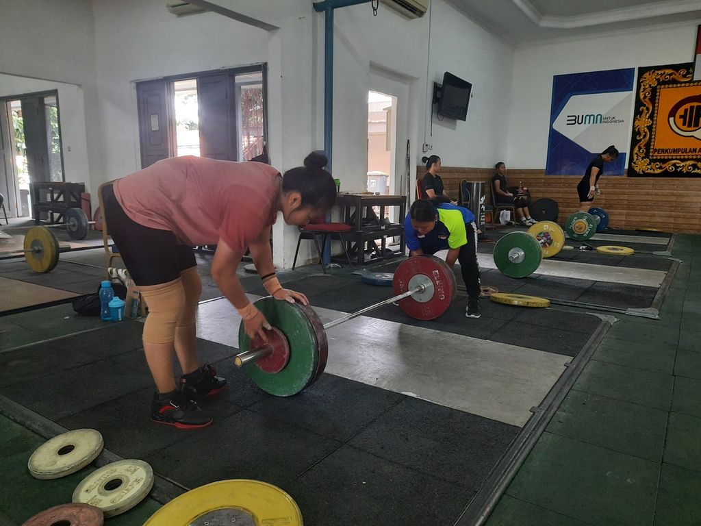 Lifter putri Restu Anggi sedang memasukkan piringan beban pada tongkat besi (barbel) saat berlatih di Mes Marinir Kwini, Jakarta, Jumat (20/1/2023). Setelah melewati babak kualifikasi pertama Olimpiade Paris 2024 di Bogota, Kolombia, pada Desember 2022, tim nasional bersiap memecah peta kekuatan untuk mengikuti SEA Games 2023 dan sejumlah babak kualifikasi Olimpiade lainnya.