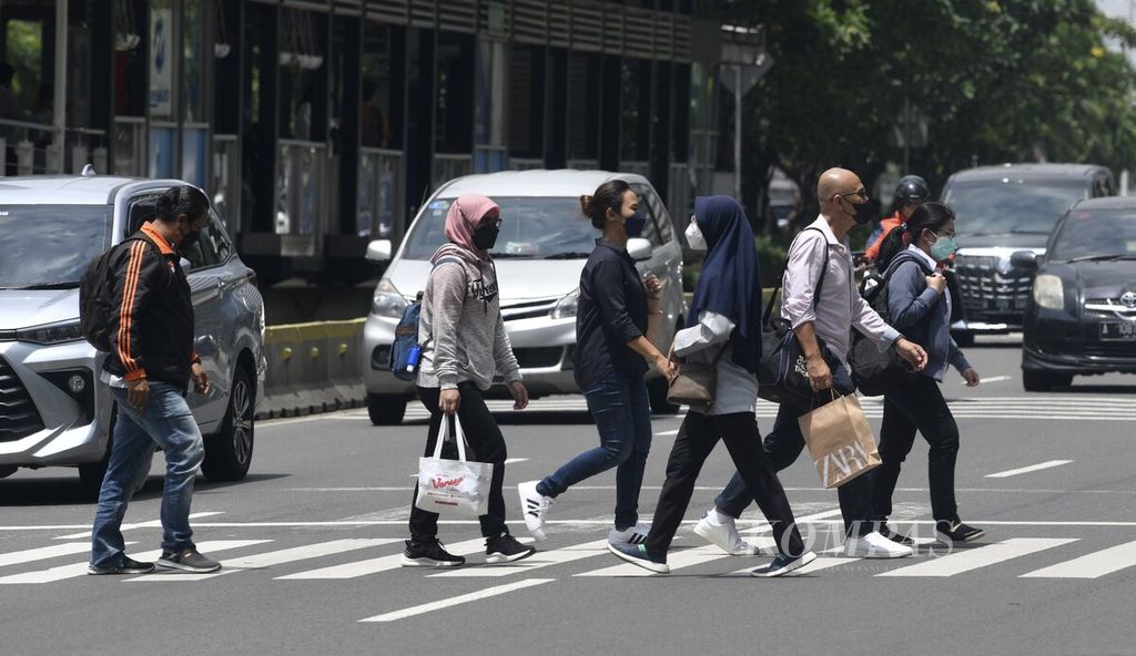 Sejumlah pekerja kantoran menyeberang di Jalan Sudirman menuju ke tempat kerja di kawasan Sudirman, Jakarta, Senin (21/2/2022).