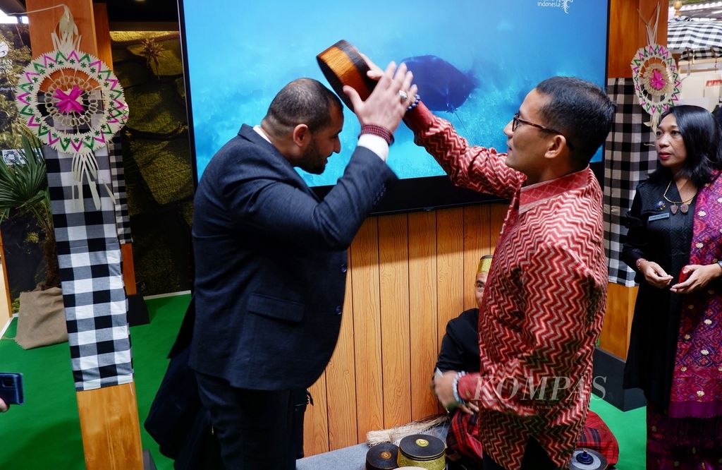 Menteri Pariwisata dan Ekonomi Kreatif Sandiaga Salahuddin Uno (kanan) memakaikan songkok recca khas Bone, Sulawesi Selatan, kepada salah seorang delegasi Tunisia, di paviliun Indonesia pada hari kedua Internationale Tourismus Borse (ITB) Berlin 2023 di Messe, Berlin, Jerman, Rabu (8/3/2023). 