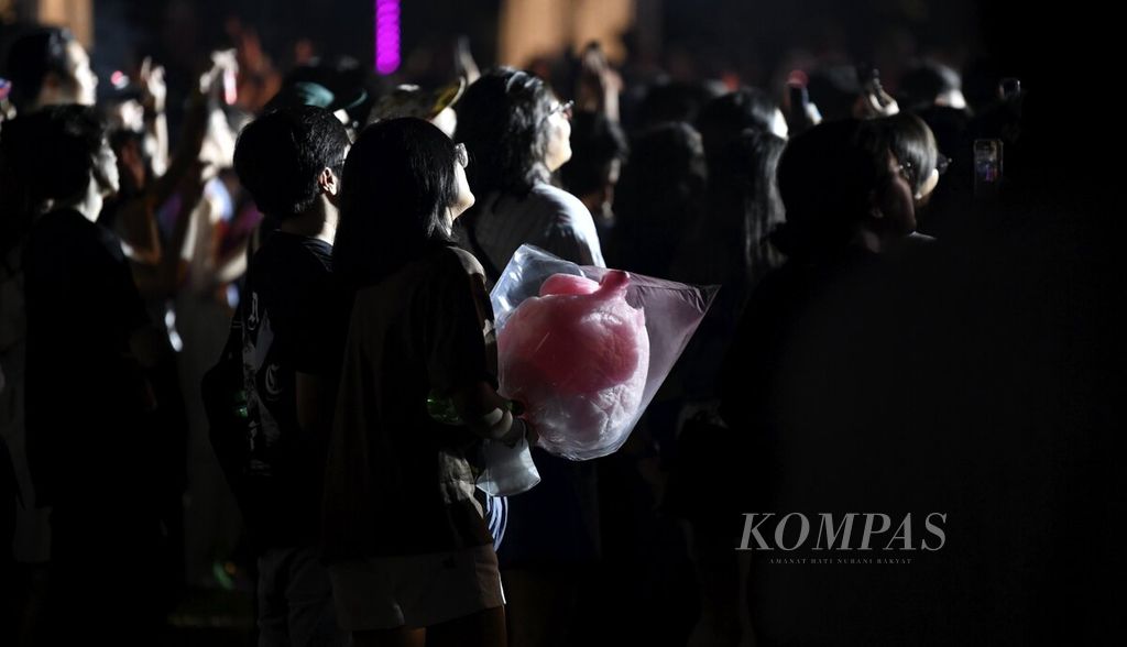 Salah seorang penonton menenteng harum manis sambil menikmati aksi panggung salah satu penampil dalam We The Fest yang berlangsung di kompleks Gelora Bung Karno, Jakarta, Jumat (21/7/2023). Festival musik We The Fest yang berlangsung selama tiga hari tersebut menghadirkan 19 musisi dan penyanyi internasional serta 25 musisi Indonesia. 