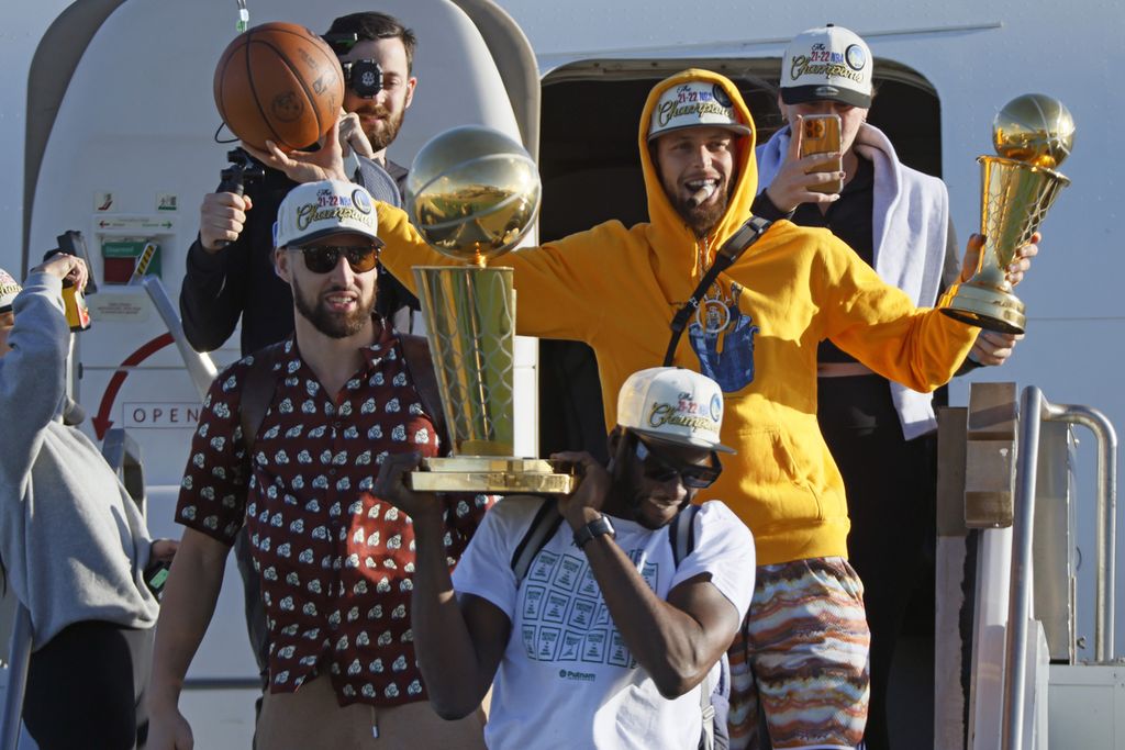 Pemain Golden State Warriors, antara lain <i>guard</i> Stephen Curry yang membawa trofi MVP Final NBA, <i>guard</i> Klay Thompson (kiri), dan <i>forward </i>Draymond Green yang membawa trofi juara NBA, keluar dari pesawat di Bandara Internasional San Francisco, California, Jumat (17/6/2022), sehari setelah mengalahkan Boston Celtics pada laga keenam Final NBA.